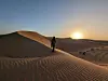 Person går på en sanddyne i ørkenen ved solnedgang