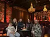 Fire kvinner og et barn sitter ved et lite bord på en dempet bar med lysekroner.