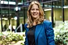 Kvinne i blå blazer står foran et kontorbygg med glass og beplantning.