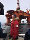Person med rød jakke og WWF-logo intervjues foran oransje oljeplattform.